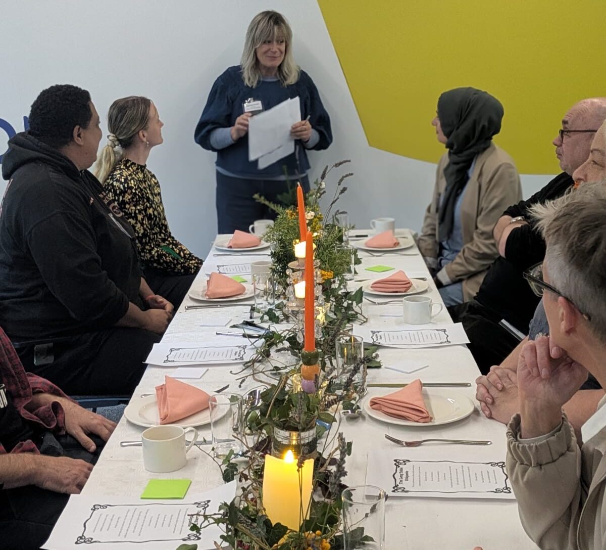 Facilitator at the top of the table explaining how the Long Table will work and attendees facing towards her listening