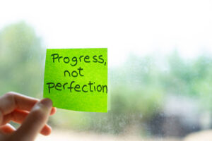 Post-it note on a window saying 'progress, not perfection'