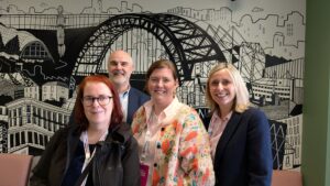 Group picture of Sam, Alex, Patsy and Nathan in front of an illustration of the Tyne Bridge in Newcastle