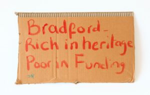 Cardboard painted with the words 'Bradford - rich in heritage, poor in funding'